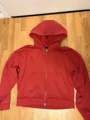 Röd hoodie med dragkedja från H&M - Säljer en röd hoodie från H&M i oversized fit. Hoodien har dragkedja framtill, stor huva och en klassisk magficka. Tillverkad i mjukt bomullsmaterial och har ribbade muddar vid ärmslut och nederkant. Perfekt för en chill och avslappnad stil.