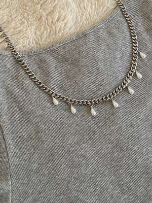 Silverfärgat halsband med pärldroppar - Snyggt halsband i silverfärgad rostfritt med kedja och små droppformade pärlor som hänger längs hela halsbandet. Perfekt för att ge en cool och elegant touch till din outfit.