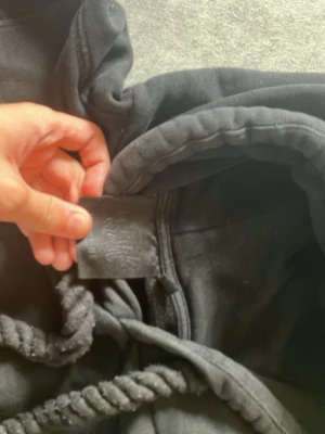 Syna world tröja  - Snygg svart hoodie med stora, grova dragsnören i luvan. Klassisk modell med rymlig huva och mjukt material, perfekt för en avslappnad streetstyle-look. Passar dig som gillar stilrena och bekväma plagg.