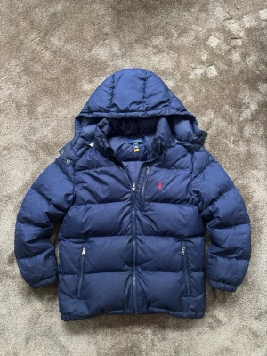 Polo Ralph Lauren dunjacka! - Säljer en snygg och varm Polo Ralph Lauren dunjacka i marinblått. Jackan är använd under en vinter och är i överlag fint skick  Storlek L 14–16, men passar även vuxen i storlek S.☺️  Det finns några mindre tecken på användning, bland annat ett litet slitage vid luvan , vilket syns på bilderna. Inget som påverkar jackans funktion eller helhetsintryck.  Väldigt fin och varm jacka som passar perfekt till höst och vinter.