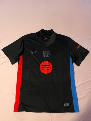 Svart FC Barcelona matchtröja Nike - Säljer en svart FC Barcelona matchtröja från Nike med röda och blå sidopaneler. Tröjan har Spotify-logga på bröstet, klubbmärke och Nike-logga. Tillverkad i lätt och ventilerande material, perfekt för fotboll eller träning.