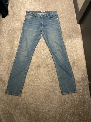 J lindeberg jeans - Säljer ett par ljusblå jeans med rak passform och klassisk femficksdesign. Jeansen har normal midja och är tillverkade i denim med subtil tvätt för en avslappnad look. Perfekta till vardags för en stilren och enkel outfit.