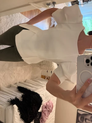 Vit puffärmad topp med struktur - Säljer en stilren vit topp med puffärmar och strukturerad passform. Toppen har korta ärmar och en något figurnära siluett som ger en modern look. Perfekt att styla med både jeans och kjol för en trendig outfit.