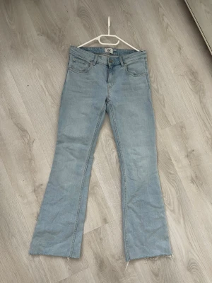 Ljusblå bootcut jeans med rå kant - Säljer ett par ljusblå bootcut jeans med rå, avklippt kant nertill. Jeansen har klassisk femficksmodell, hög midja och är tillverkade i denim. Perfekta för dig som gillar en avslappnad och trendig stil.