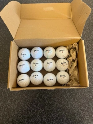 Srixon vita golfbollar i kartong - Ett set med vita golfbollar från Srixon, levereras i en kartong. Bollarna har siffror och Srixon-logga tryckt i svart och rött. Klassisk rund form och tillverkade i slitstarkt material som passar perfekt för golfbanan.