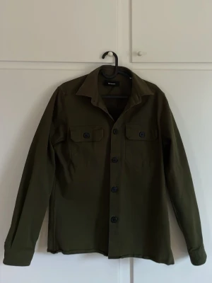 Olivgrön overshirt från Gabba - Snygg olivgrön overshirt från Gabba, nyskick. Köpte sent på hösten 2025. Endast använd två gånger. Perfekt att använda om man vill ha en skön och snygg overshirt. Nypris 1000 kr