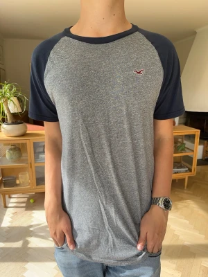 Hollister T-shirt grå blå herr  - Hollister raglan t-shirt med snygg färgkombination. Gråmelerad kropp med kontrasterande mörkblå ärmar. Väldigt mjukt tyg och i mycket fint skick. Enkel att styla till vardags!Märke: HollisterSkick: Fint skick#hollister #raglan #herr #tshirt #grå #blå #vardag #streetwear #vinted #basplagg