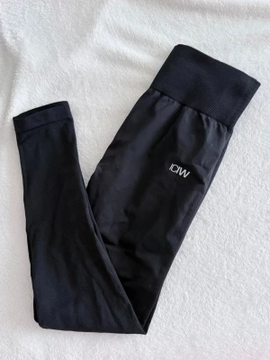 Svarta leggings från ICANIWILL - Snygga svarta leggings från ICANIWILL med hög midja och bred ribbad linning. Tillverkade i stretchigt material som sitter skönt och formar sig efter kroppen. Diskret logga på låret. Perfekta för träning eller chill.