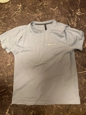 Ljusblå Sail Racing t-shirt - Ljusblå t-shirt från Sail Racing med rund hals och korta ärmar. Tryckt logga i vitt på bröstet. Skön och stilren modell, perfekt till jeans eller shorts. Troligtvis i bomullsmaterial.