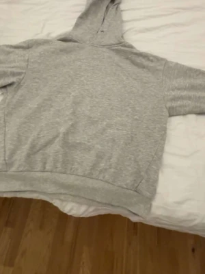 Ljusgrå hoodie från 157 - En enkel och stilren ljusgrå hoodie från 157 i storlek S. Hoodien har en klassisk huva och ribbade muddar vid ärmslut och nederkant. Perfekt för en avslappnad look och passar till det mesta. Mjuk och skön bomullsblandning.