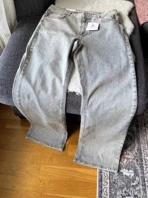 Gråa wide leg jeans med hög midja - Säljer ett par jättefina ljusgrå jeans "Never Denim"-kollektion i modellen Mid Wide 950. Sitter superfint med medelhög midja och trendiga vida ben. De har "comfort stretch" vilket gör dem väldigt sköna att bära!Märke: Never Denim Modell: Mid Wide 950Storlek: 34 i midja / 32 i längdPassform: Mid waist, wide leg, comfort stretch.   Helt nya, med etiketter kvar