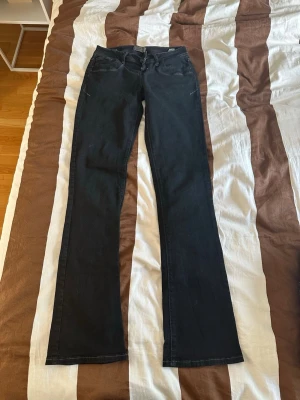 Svarta bootcut jeans - Säljer ett par svarta bootcut jeans med klassisk femficksdesign och dragkedja framtill. Jeansen har en snygg passform som är smal upptill och utsvängda nedtill. Perfekta för dig som gillar en tidlös och cool look. Lågmidjade, storlek 26/34