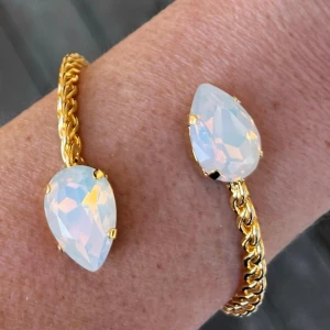 Bangle armband White Opal kristall  - Armband, Bangle, i guldpläterad mässing med kristaller. Kristaller Pear 18mm. Färg White Opal, ställbar storlek. De senare bilderna andra armband som finns i lager. Jag skickar endast spårbart, samfraktar. Fast pris. Besök gärna mina övriga annonser.  Till mina smycken använder jag kristaller från Preciosa, Aurora och Swarowski.