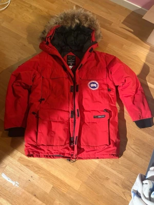 Röd Canada Goose Expedition Parka - Säljer en röd Canada Goose Expedition Parka i nyskick! Nedärvd av en familjekompis och knappt använd, dock har spännena runt midjan gått sönder lite, se bild 7.                                                          Perfekt för kyliga höst-vinterdagar och riktigt varm. Skriv vid minsta fråga eller fundering, priset är självklart förhandlingsbart!❄️🧣🍁