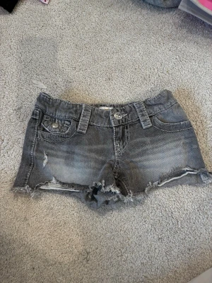 Grå  jeansshorts med brodyr - Snygga grå jeansshorts med slitna detaljer och fransig kant. Shortsen har fem fickor, bälteshällor och coola broderier med paljetter på bakfickorna. Perfekta för en avslappnad och trendig look.