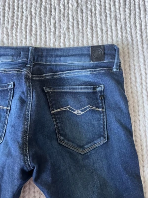 Blå slim jeans från Replay - Snygga blå jeans från Replay med klassisk femficksdesign och smal passform. Jeansen har tydliga kontrastsömmar och en mörk tvätt med lätt slitning. Perfekta för en trendig och avslappnad look.