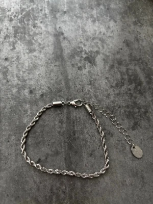 Tunt silverfärgat tvinnat armband - Snyggt och stilrent armband i silverfärg med tvinnad kedja och justerbar längd tack vare förlängningskedjan. Armbandet har en liten bricka vid låset och passar perfekt för dig som gillar minimalistiska accessoarer.