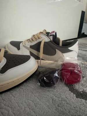 Nike Jordan travisscott  - Nike Jordan travisscott  Snygga sneakers i grått och vitt med beige detaljer och matchande beige skosnören. Skorna har en låg silhuett och kommer med extra skosnören i svart och rött. Perfekta för dig som vill ha en clean och stilren look.