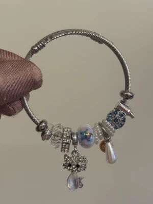 Silverfärgat armband med berlocker - Stilrent armband i silverfärgad metall med flera dekorativa pärlor och berlocker. 
