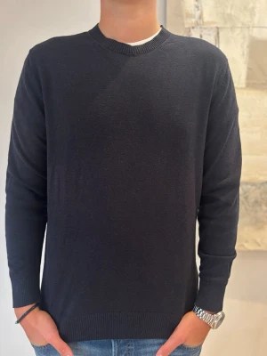 Svart rundhalsad tröja - En stilren svart tröja med rund halsringning och långa ärmar. Tröjan har ribbade muddar vid ärmslut och nederkant, och är tillverkad i ett mjukt material som passar perfekt till jeans. Enkel och klassisk design utan synliga loggor eller mönster. 