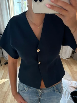 Mörkblå topp med v-ringning och knappar - Snygg mörkblå topp från ZARA med v-ringad hals och två guldfärgade knappar framtill. Nästan helt ny.