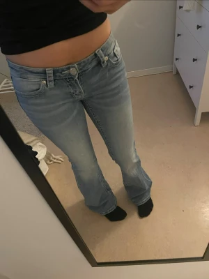 Ljusblå bootcut jeans med broderi - Snygga ljusblå jeans med bootcut-modell och coola broderade detaljer på bakfickorna. Jeansen har klassisk femficksdesign och är tillverkade i denim med lätt tvättad look. Perfekta för dig som gillar en avslappnad men trendig stil. har lite slitage i benen som man ser på sista bilderna!!! i storlek S