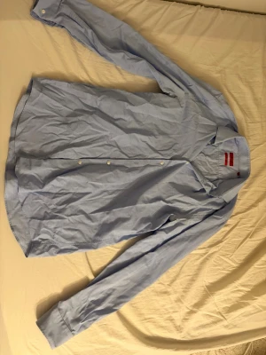 Ljusblå skjorta från Hugo Boss - Säljer en stilren ljusblå skjorta från Hugo Boss i storlek 43 (Slim Fit). Skjortan har ett elegant mönster med små vita prickar som ger ett exklusivt och modernt utseende. Perfekt för både jobb, fest och mer uppklädda tillfällen. Skjortan är i fint skick utan hål eller fläckar.