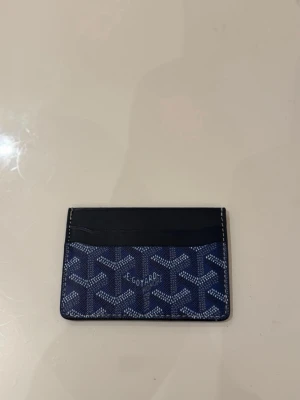 Blått korthållare  - Snygg blå korthållare, ikoniskt mönster och svarta detaljer i skinn. Perfekt för kort och ID, smidig att ha i fickan. Klassisk design med flera kortfack och stilren look.