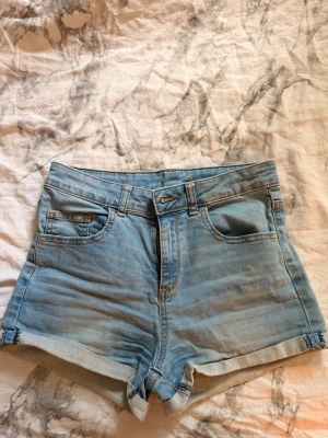 Ljusblå denimshorts  - Snygga ljusblå denimshorts med hög midja och uppvikta benslut. Perfekta för varma dagar och enkel att matcha med olika toppar. Vet inte rikigt vart de är ifrån medan tror kappahl. 