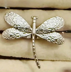 Silverfärgad ring med trollslända - Unik ring i silverfärgad formad som en trollslända. Vingarna har ett detaljerat, texturerat mönster som ger en cool och naturinspirerad look. Perfekt för dig som gillar smycken med djurmotiv och vill sticka ut lite extra.