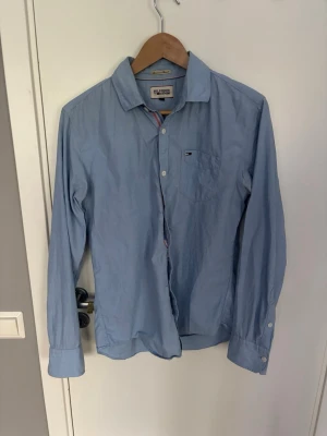 Ljusblå skjorta från Hilfiger Denim - Säljer en klassisk ljusblå skjorta från Hilfiger Denim. Skjortan har lång ärm, knappstängning och en bröstficka med liten logga. Tillverkad i mjuk bomull och har diskreta randiga detaljer på insidan av kragen och knappslån. Skjortan är använd fåtal gånger och är i ett mycket bra skick, hör av er vid frågor!