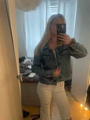 Klassisk blå jeansjacka - Säljer en klassisk blå jeansjacka i tidlös modell. Jackan har två bröstfickor med lock och knappar framtill. Passformen är rak och jackan har en snygg tvättad look som passar till det mesta. Perfekt att slänga över en t-shirt eller hoodie.