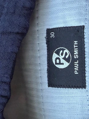 Mörkblå  byxor från Paul Smith - Säljer ett par mörkblå byxor från Paul Smith med snörning i midjan. Shortsen har en avslappnad passform och är tillverkade i ett svalt tyg, perfekt för varma dagar. Detaljerad med blå och bruna snören för extra stilpoäng.