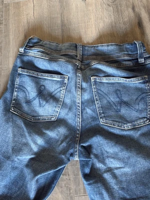 Gina jeans - Endast använd några gånger. Säljer ett par klassiska blå jeans med raka ben och snygga broderade detaljer på bakfickorna. Jeansen har fem fickor, bälteshällor och stängs med dragkedja och knapp. Tillverkade i slitstark denim som ger en avslappnad look.