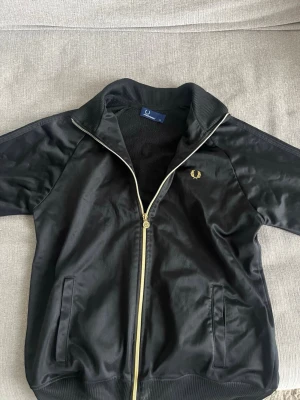 En zip hoodie från fred Perry - Säljer denna zip hoodie från fred Perry som är i färgen svart med lite guld detaljer på dragkedjan. Använt ett fåtalgånger cirka 1-4. Kan gå ner i pris i en snabb och smidig affär! Köparen står för frakten😁