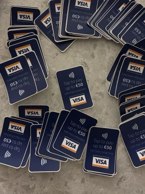 Visa kontaktlösa betalningssklistermärken - Bor du i en storstad? Gå till varje affär och fråga om de vill köpa klistermärken av dig! ;) Ett gäng rektangulära skyltar i hård plast med blå bakgrund och texten 'Tap to pay up to €50 with Visa contactless'. Perfekta för att visa att kontaktlös betalning accepteras. Klassisk Visa-logga i vitt, blått och orange längst ner på skylten.