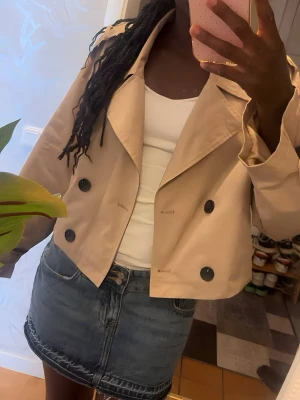 Kort beige trenchcoat i croppad modell – Storlek M - Säljer en otroligt snygg och modern trenchcoat i en kortare, croppad modell. Den perfekta vår- och höstjackan som lyfter vilken outfit som helst! Tack vare den korta passformen är den superfin  Helt ny endast använt 1 gång  Skriv gärna om du har några frågor eller vill ha fler bilder! Fraktar snabbt.🩷  Längd: ca 45–48 cm (croppad modell)Bystvidd: ca 100–104 cm (runtom)Ärmlängd: ca 60–61 cm
