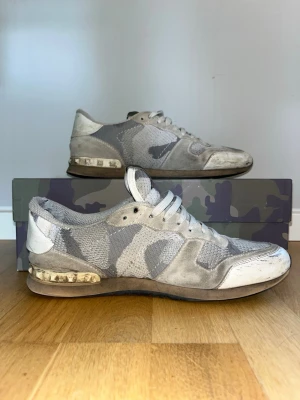 Valentino rockrunners - Snygga sneakers från Valentino med grå och vit camo-mönster. Skorna har mesh och mockadetaljer, vita skosnören och en unik sula med transparent detalj. Perfekta för dig som vill sticka ut med stilrena men ändå coola skor. Skorna kommer med skolåda och dustbag. Det finns en skada på vänstra skon som man ser på bild 7 och så börjar sulan tunna ut vid hälen av båda skor därför säljer jag dem för bara 600.