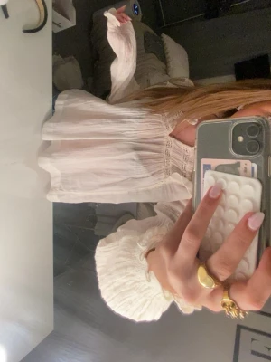 Vit blus med lång ärm - Söt vit blus med romantiska detaljer och smockad midja. Blusen har långa, puffiga ärmar med resår vid ärmslut och en luftig, flowy passform. Perfekt för en trendig och feminin look.
