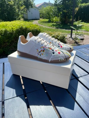 Maison Margiela skor - blandad färg - Unika vita sneakers med färgstänk i rött, gult, blått och svart. Skorna har klassisk låg profil, vita snören och beige sula. Materialet mocka, endast testade.
