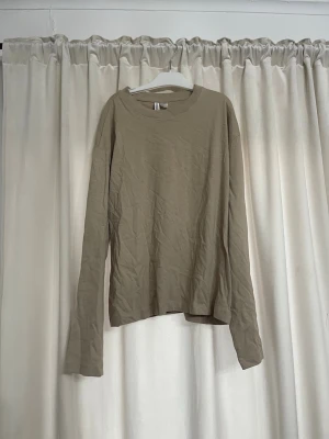 Beige långärmad basic tröja - En enkel beige långärmad tröja i mjukt material. Tröjan har rund halsringning och rak passform, perfekt för lager på lager eller som basplagg till olika outfits. Men breda armar 