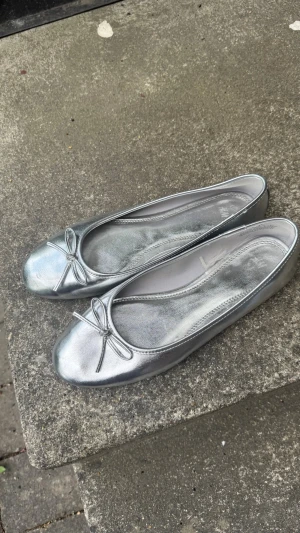H&M Silvriga ballerinaskor med rosett - Snygga ballerinaskor i metallic-silver med rund tå och liten rosett framtill. Skorna har en klassisk och stilren design med glansig finish och mjukt material som ger en bekväm känsla. Perfekta för att lyfta vilken outfit som helst. Från H&M ALDRIG ANVÄNDA pris går att diskutera!!!!