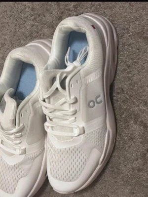 On cloud skor  - Snygga vita sneakers från On med ventilerande meshpaneler och klassisk snörning. Skorna har en chunky sula och diskret logga på sidan. Insidan är ljusblå för extra stilpoäng. Perfekta för dig som gillar sportig och clean look.