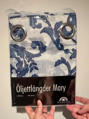 Öljettlängder Mary blåvit Solbacka - Säljer ett par öljettlängder Mary från Solbacka i blåvitt blommigt mönster. Gardinerna är 140x240 cm och tillverkade i 100% polyester. Perfekt för att ge rummet en fräsch och stilren känsla med metallöljetter för enkel upphängning.