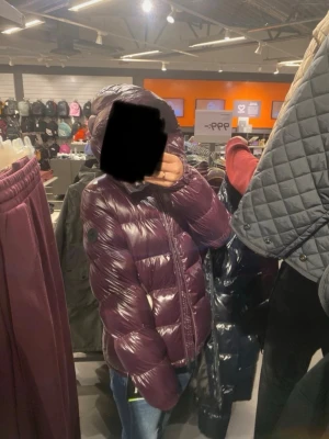 Vinter jacka - Snygg och trendig mörklila dunjacka med glansig finish och huva. Jackan har quiltad design, dragkedja framtill och en patch på ärmen. Perfekt för kalla vinterdagar och ger en cool streetstyle-look.