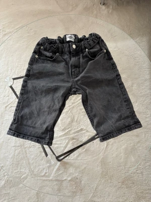 Svarta jeans från 157 Shorty Star - Säljer ett par svarta jeans från 157 Shorty Star med resår i midjan och klassisk femficksmodell. Jeansen har raka ben och knappgylf. Perfekta för en avslappnad och cool stil.