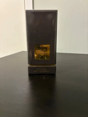 Tom Ford Tobacco Vanille EdP - Tom Ford Tobacco Vanille Eau de Parfum i en elegant mörkbrun rektangulär flaska med guldfärgad etikett. Doften kombinerar varma toner av tobak och vanilj för en lyxig och unik parfymupplevelse. Förpackningen har exklusiv känsla och passar dig som gillar djupa, kryddiga dofter.