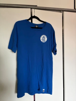 Blå t-shirt från Frank Dandy - Snygg blå t-shirt från Frank Dandy med rund hals och tryckt logga på bröstet. 