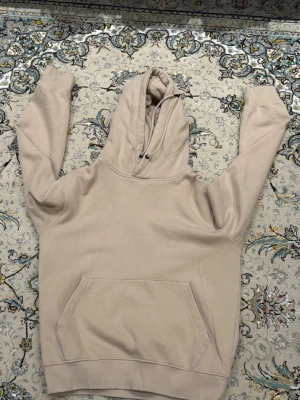 Beige hoodie från Jack and Jones  - Säljer en stilren beige hoodie med klassisk huva och dragsko. Hoodien har en stor magficka framtill och ribbade muddar vid ärmslut och nederkant. Perfekt för en avslappnad och trendig hoodie, storlek xs men passar S bättre 
