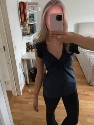 Mörkblå omlottopp med volangärm - Snygg mörkblå topp med omlottdesign och djup v-ringning. Toppen har korta volangärmar som ger en feminin touch och är tillverkad i ett mjukt bomullsliknande material. Perfekt att styla med jeans eller kjol för en trendig look.
